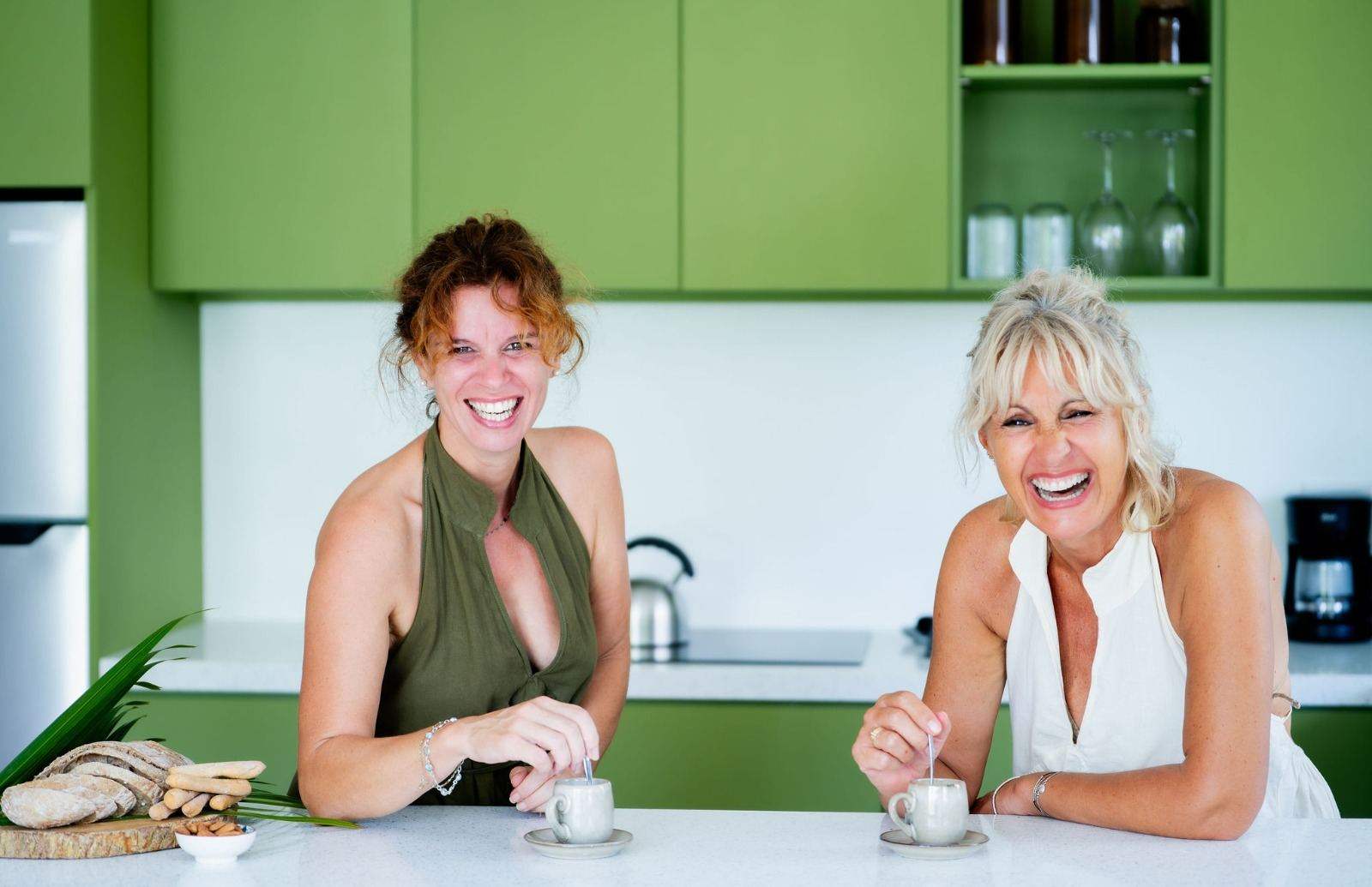 Elisabetta and Silvia laughing over coffee in a green kitchen